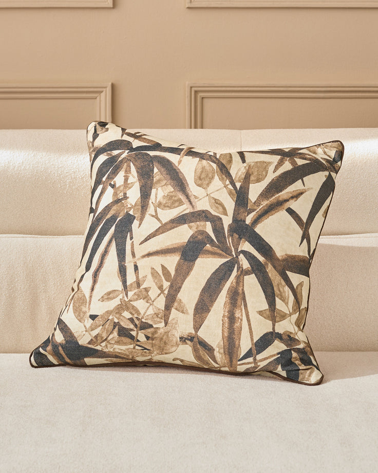 Madeira Cushion in natural tones featuring a botanical leaf pattern in charcoal and taupe on cream, displayed on a beige sofa.