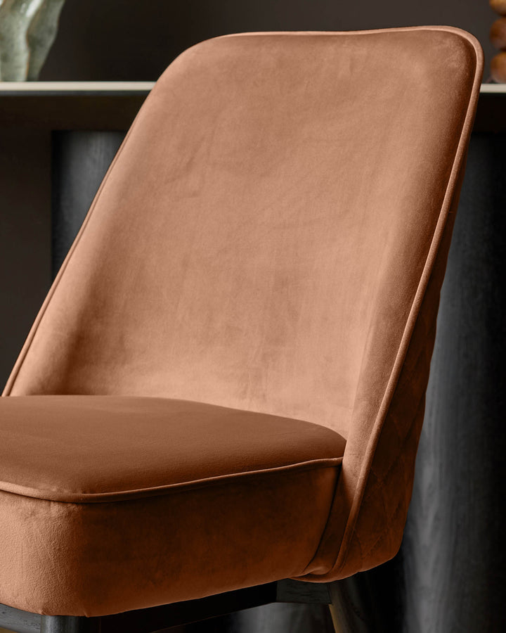 Mae velvet dining chair in rust, shown at an angle highlighting the curved backrest and upholstered seat.