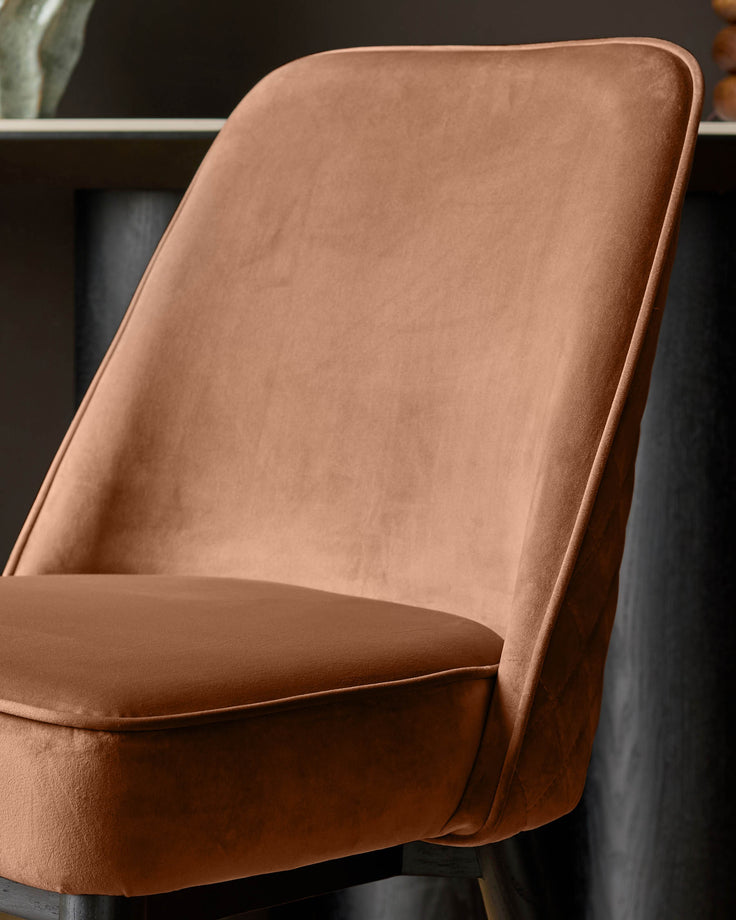 Mae velvet dining chair in rust, shown at an angle highlighting the curved backrest and upholstered seat.