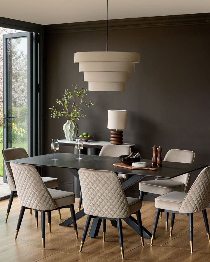 Mae velvet dining chair in champagne, shown in a styled dining room setting with quilted backrest and brass-tipped legs.