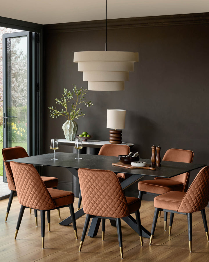 Mae velvet dining chair in rust, featuring quilted backrest, black legs with brass feet, shown in modern dining room setting.