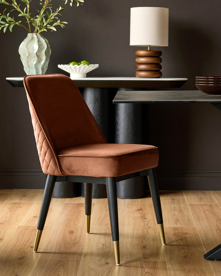 Mae rust velvet dining chair with quilted backrest and black wooden legs with brass feet.