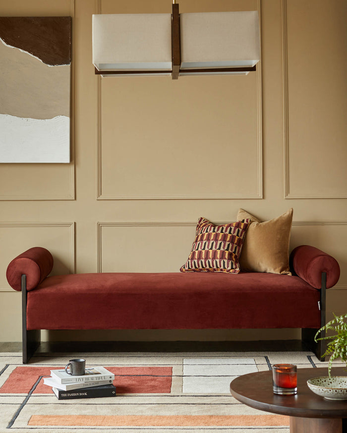 A plush red velvet bench with roll cushions and a patterned rug adds warmth and style to this inviting living space.