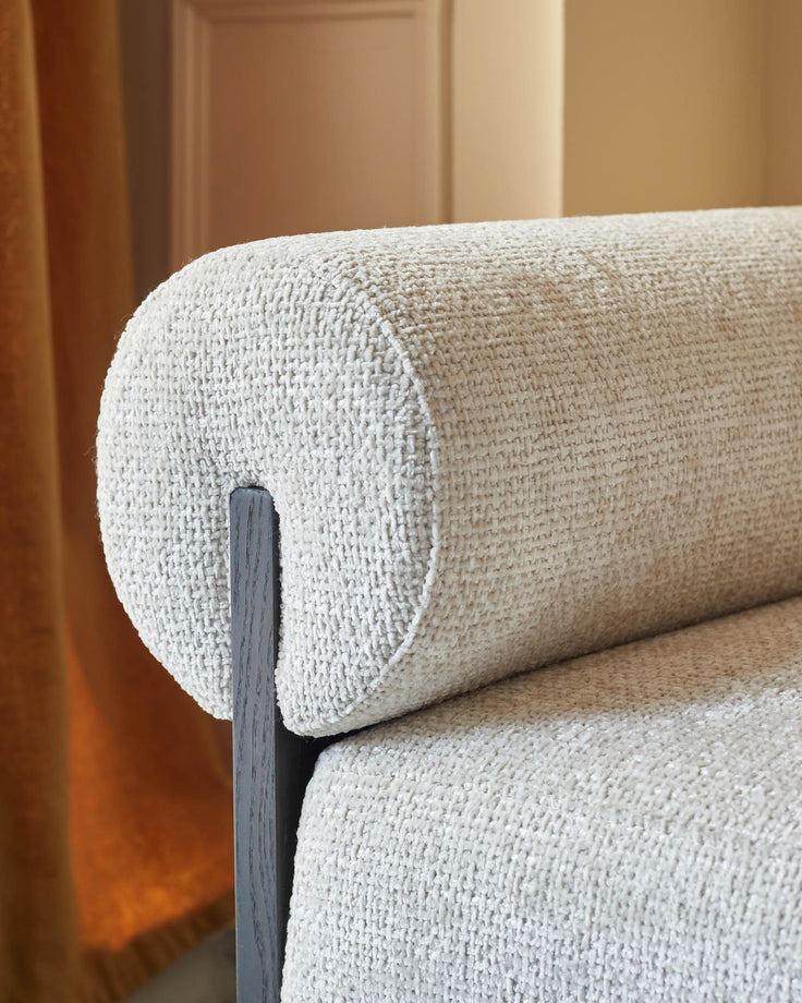 Close-up of an armrest with light textured fabric, supported by dark wooden frame. Stylish furniture piece.