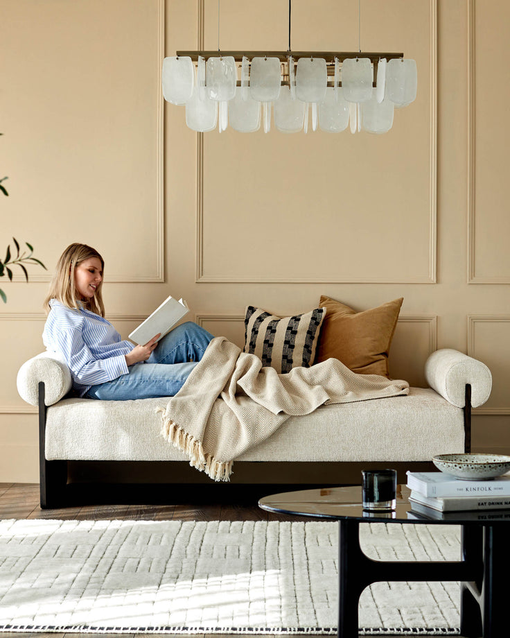 Stylish cream sofa with decorative pillows, throw and black table, under a unique, modern light fixture. Ideal for a cosy, modern home.