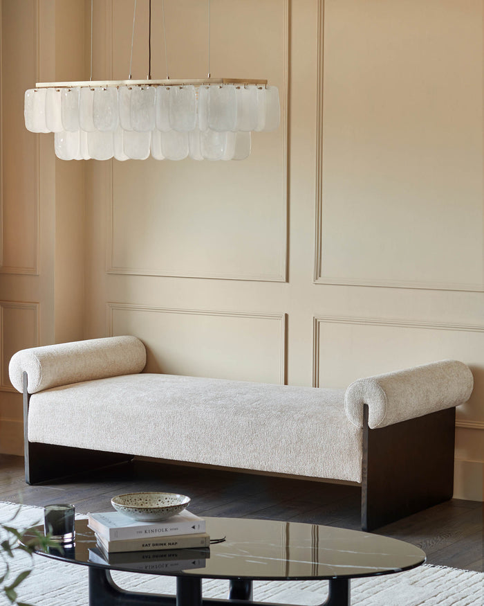 Stylish daybed with roll cushions, dark wood base, and a modern chandelier. Elegant living room furniture.