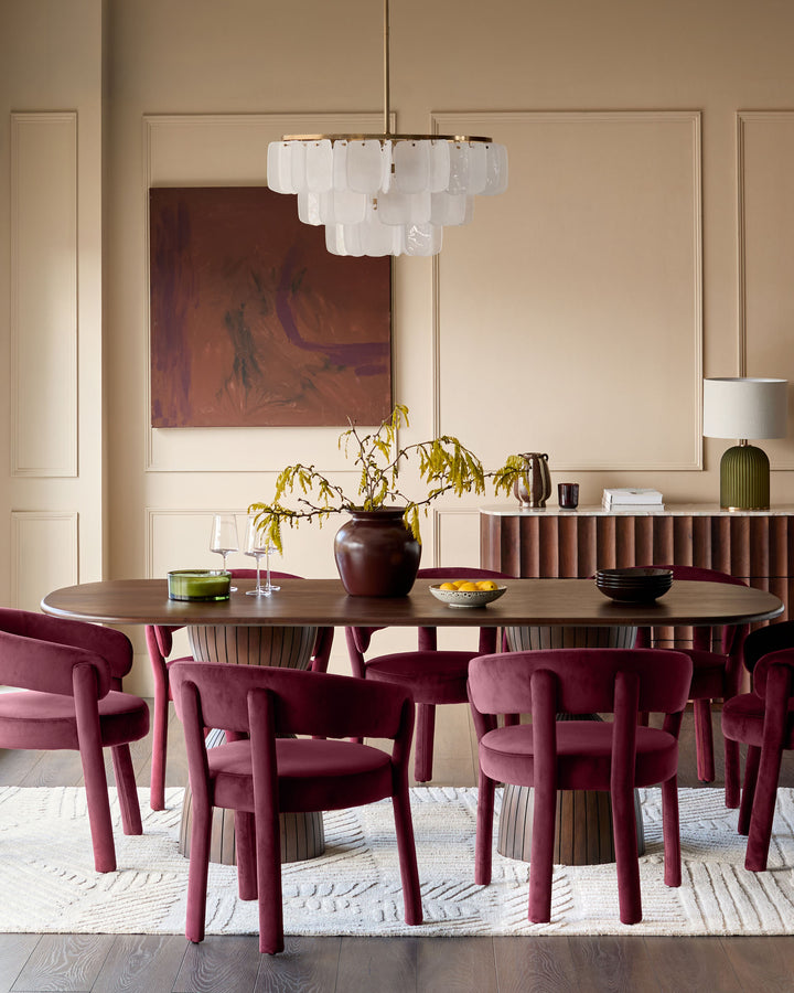 Malin 8-seater dining table in dark mango wood with oval top, shown in styled dining room setting with burgundy chairs.