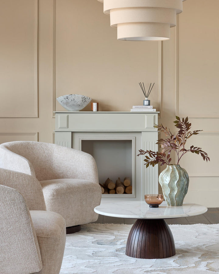 Malin round coffee table with white marble top and dark mango wood pedestal base, styled in a modern living room.