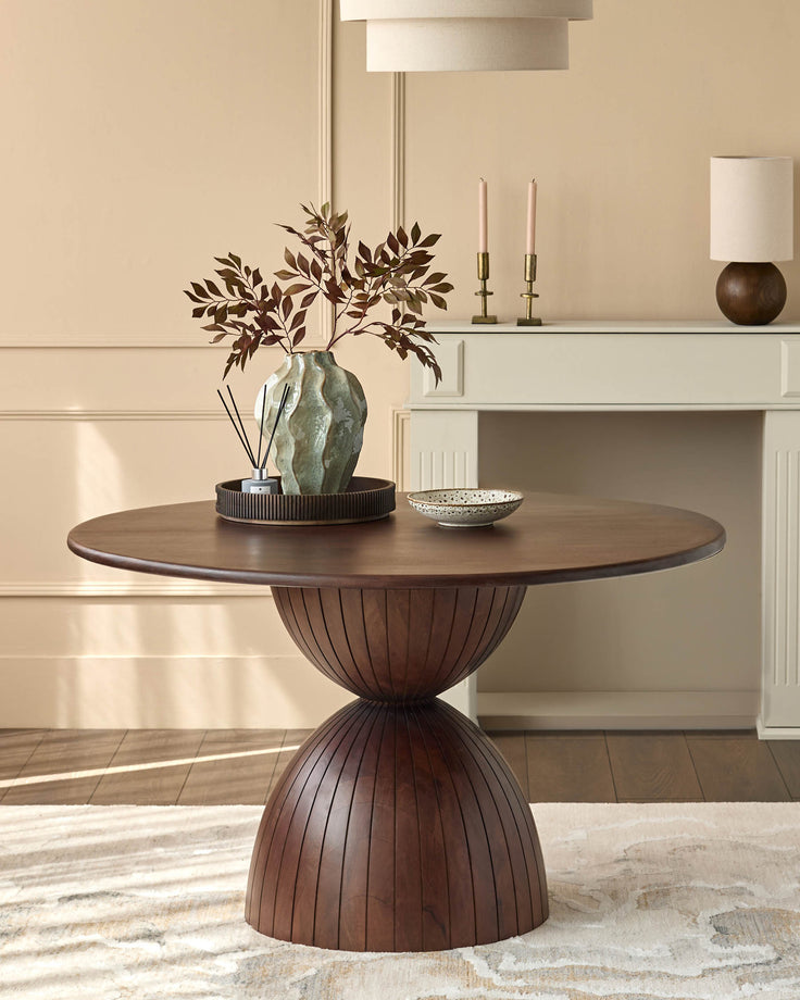 Dark mango wood round dining table with fluted pedestal base, styled with dried botanical arrangement and decorative bowl.