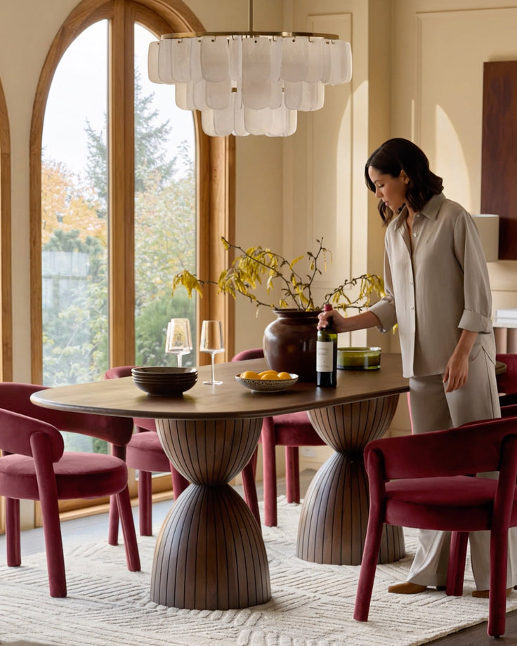 Dark mango wood round dining table with pleated pedestal base, styled with burgundy chairs in a bright dining room.