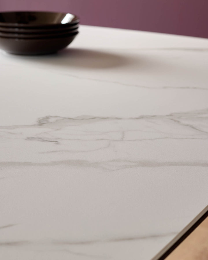 White marble-effect ceramic dining table top with black bowls, purple wall background, angled view showing surface texture.