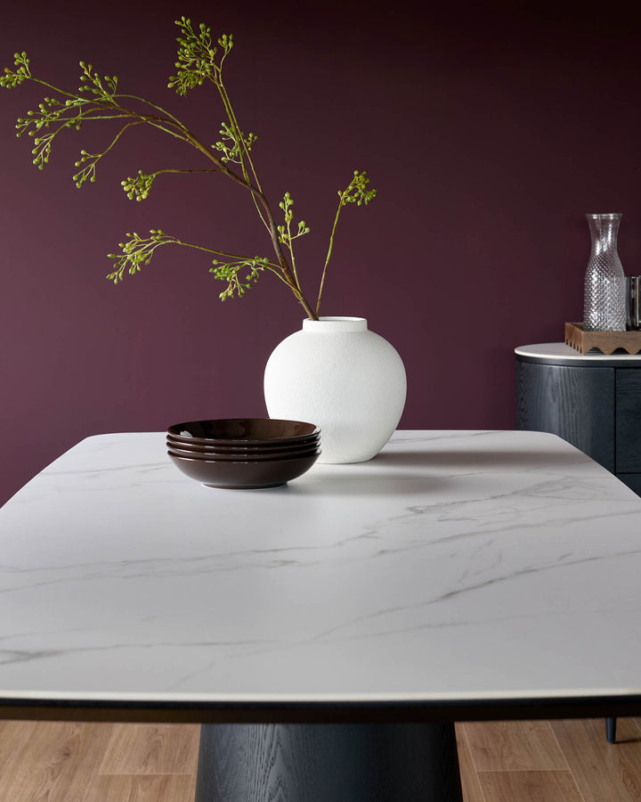 Manhattan 8-seater dining table with white ceramic top and dark wood pedestal base, styled with bowls and floral vase.