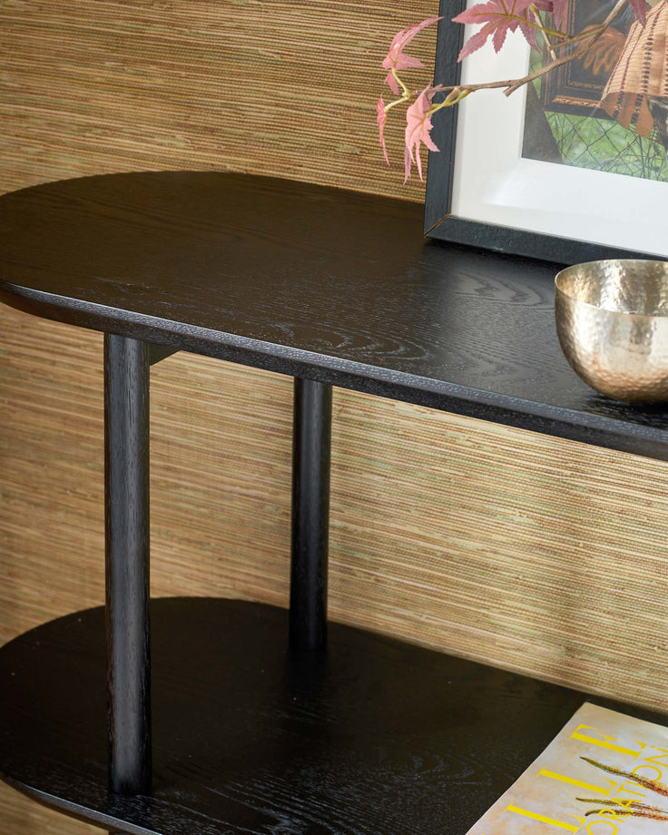 A dark, two-tiered side table with rounded shelves, displaying decorative items and a magazine.
