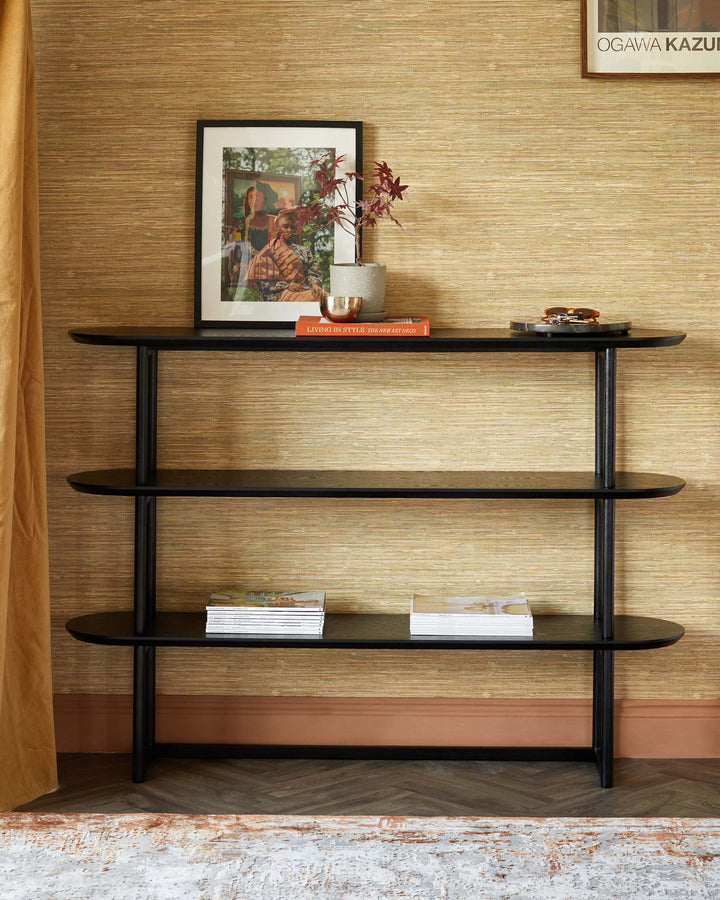 A three-tiered black console table displays books and ornaments against a textured wall and parquet flooring.