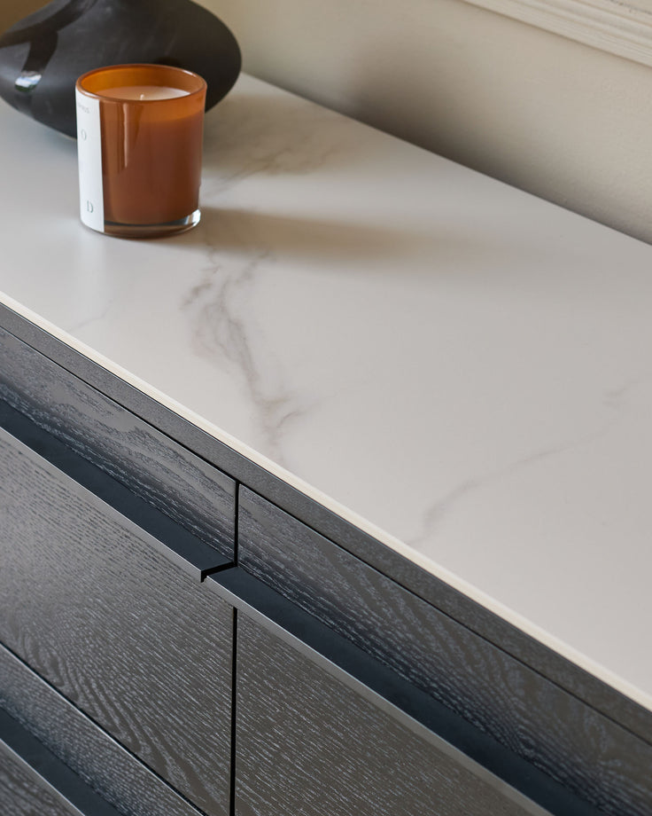 Manhattan 6-drawer chest in ceramic white with black wood base, minimalist metal handle detail visible.
