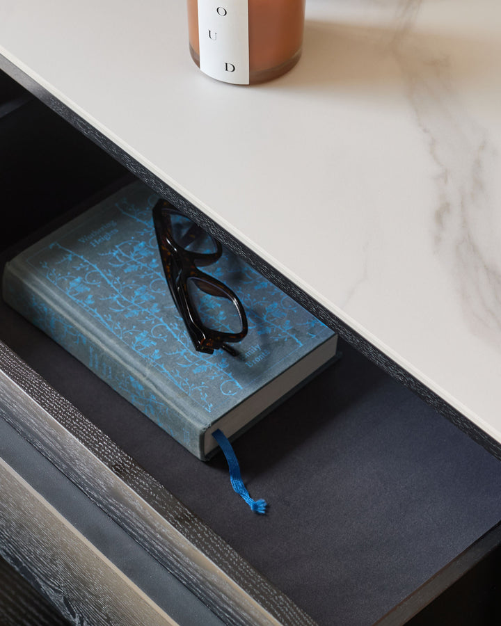 Manhattan 6-Drawer Chest in ceramic white with dark wood-grain frame, styled with books and decorative objects on top.