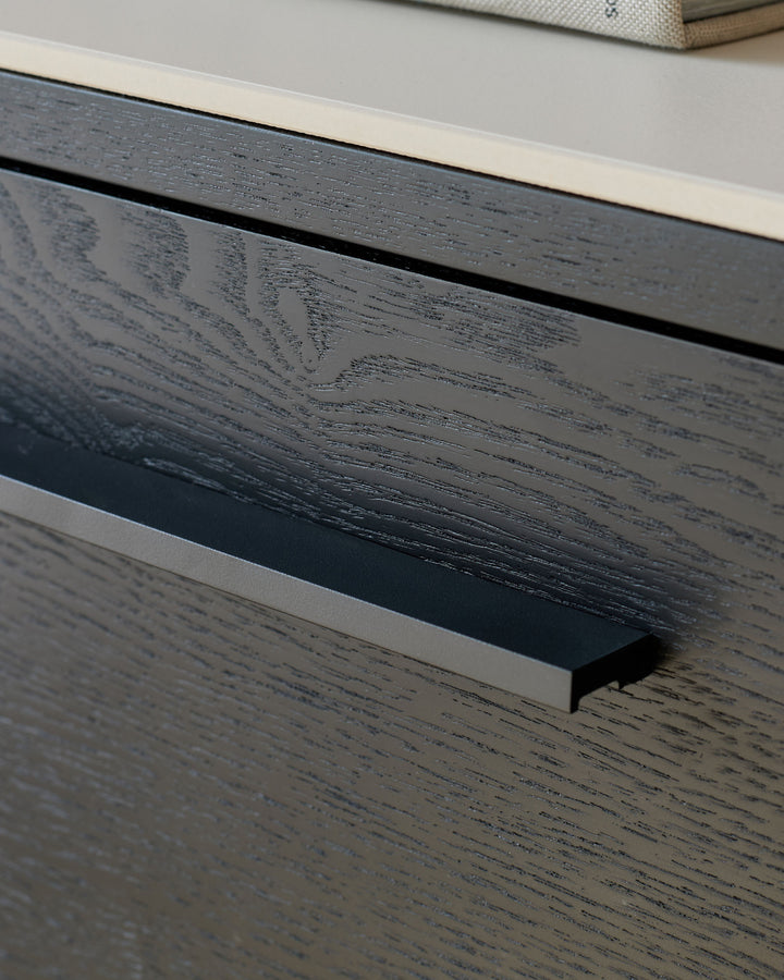 Black wood drawer handle detail on white ceramic dresser, close-up side view.