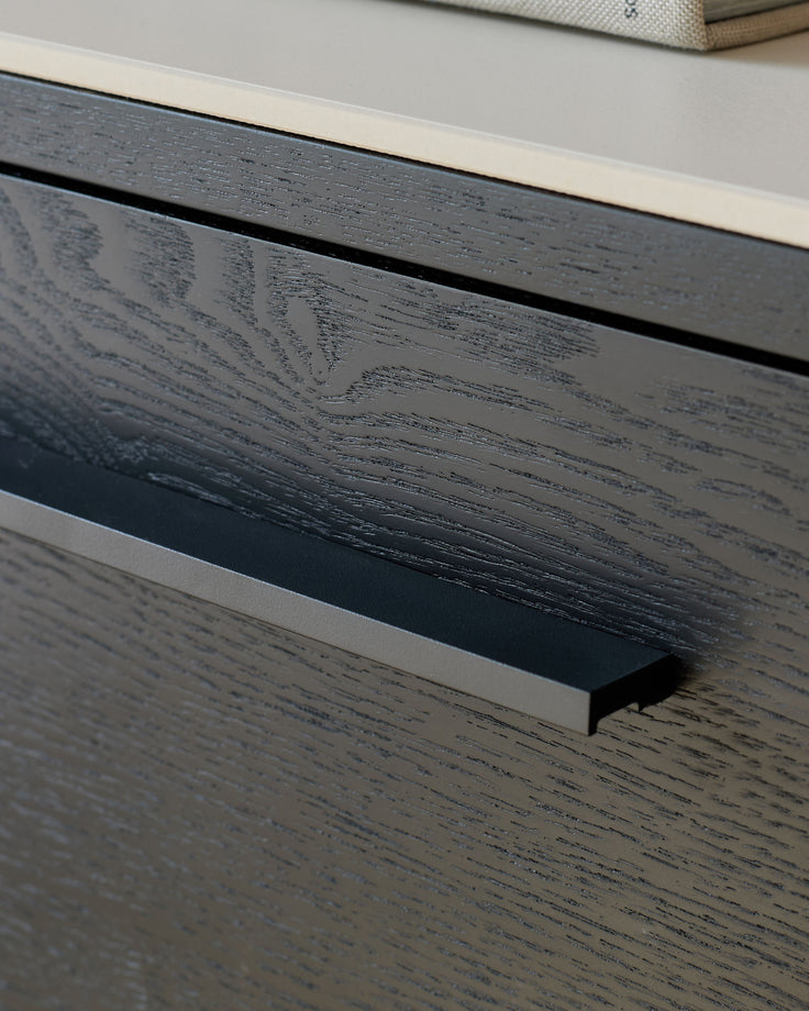Black wood drawer handle detail on white ceramic dresser, close-up side view.