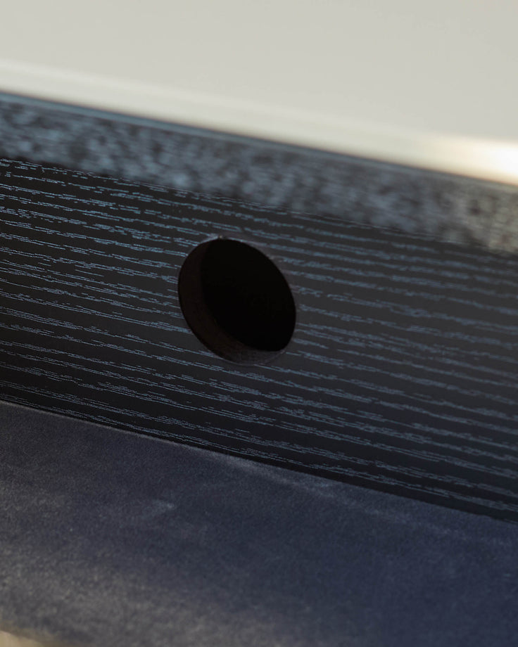 Black wooden bedside table with textured finish, showing detail of round dark handle against wood grain surface.
