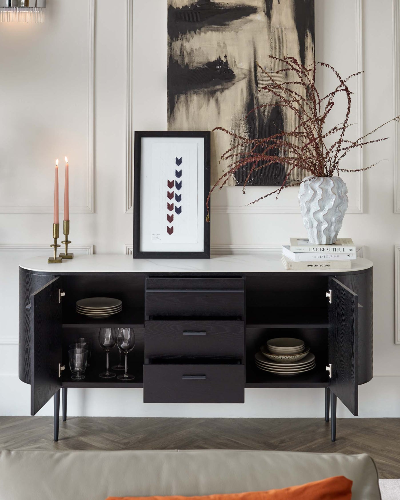 Elegant contemporary sideboard in a dark finish with textured front panels. Features include two doors revealing shelved storage spaces, three central drawers for additional storage, and stylish tapered metal legs. Accessories and tableware on display are not included.