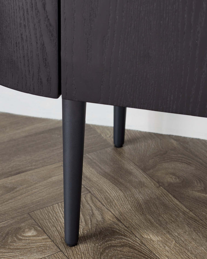 Modern minimalist dark-stained wooden cabinet with sleek, straight-line design and cylindrical black metal legs on a textured hardwood floor.