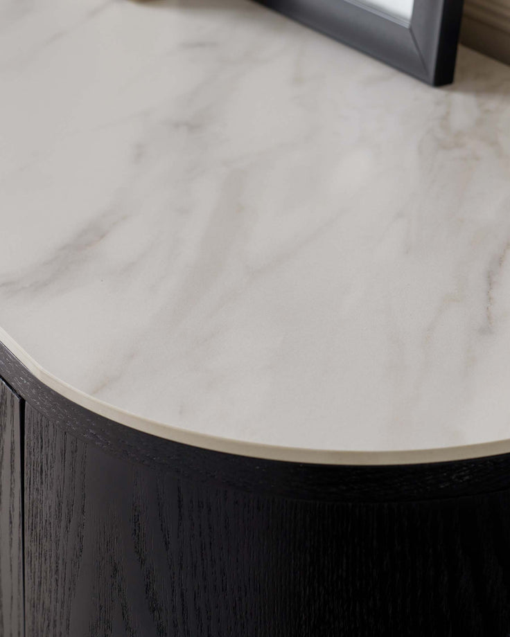 A close-up view of a refined round corner of a table featuring a luxurious white marble top and an elegant dark wooden base with a visible wood grain texture.