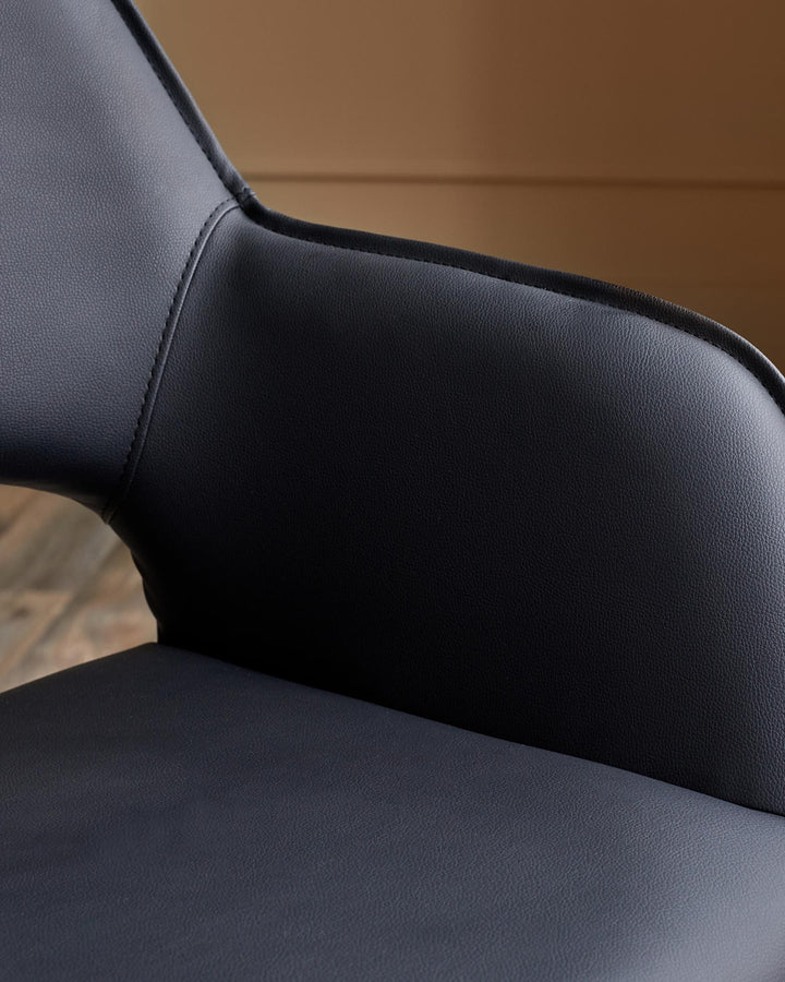 Close-up of a modern, black leather chair, showing the seat and backrest with detailed stitching.