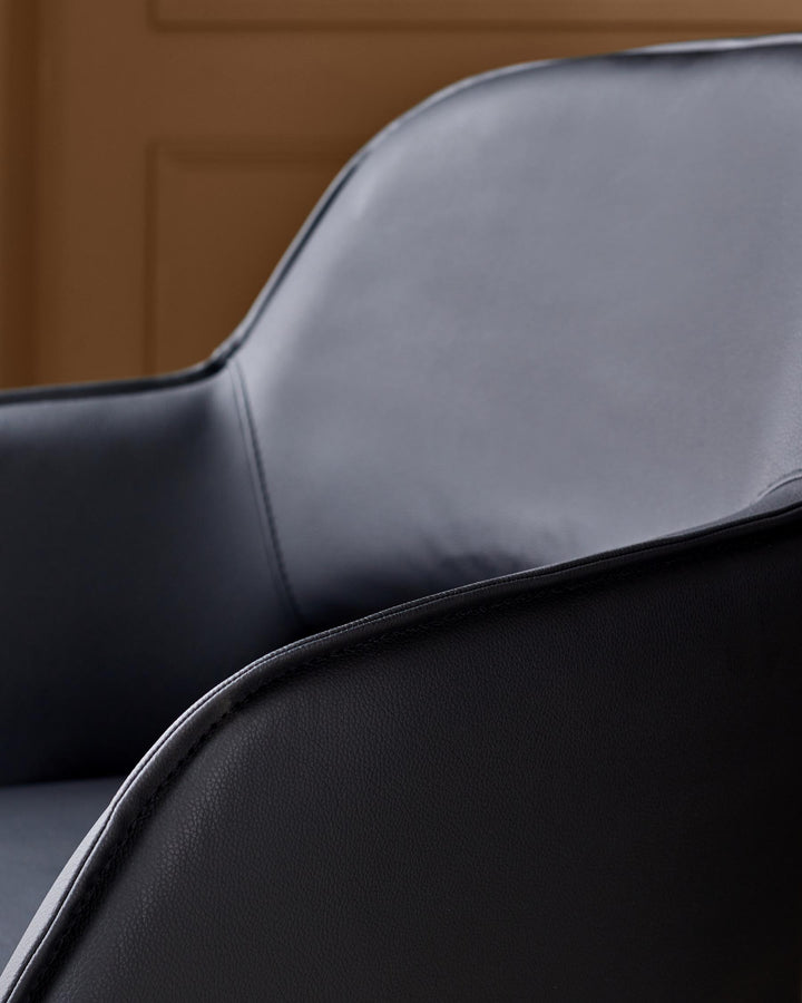 Close-up of a black leather chair with a curved back and armrests. The chair has a modern, minimalist design.