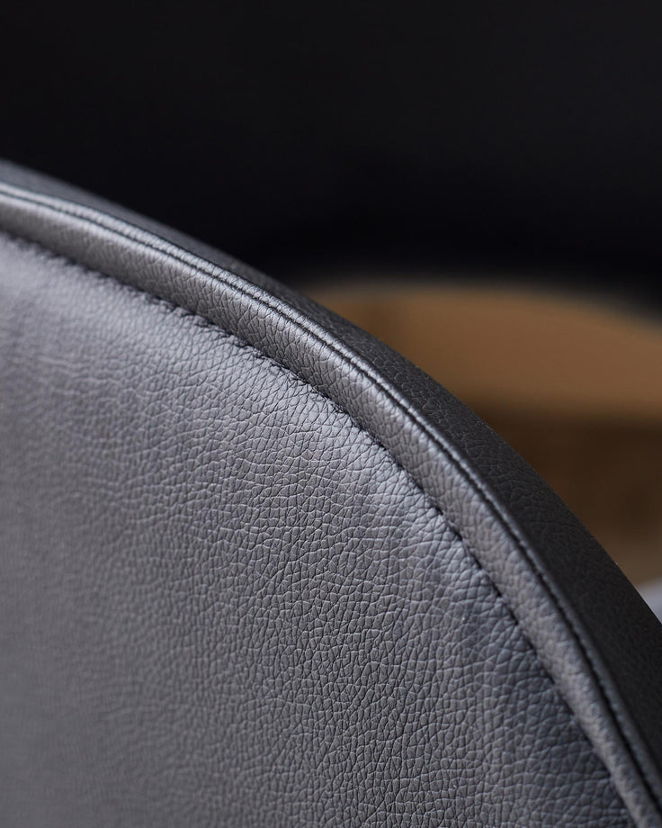 Close-up of a sleek, black leather chair showing its texture and elegant stitching detail.