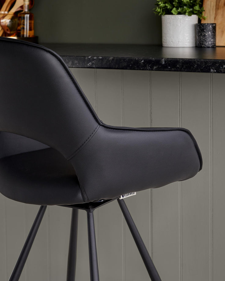 Close-up of a sleek, black bar stool, showcasing its modern design and comfortable, armrest-equipped seat.