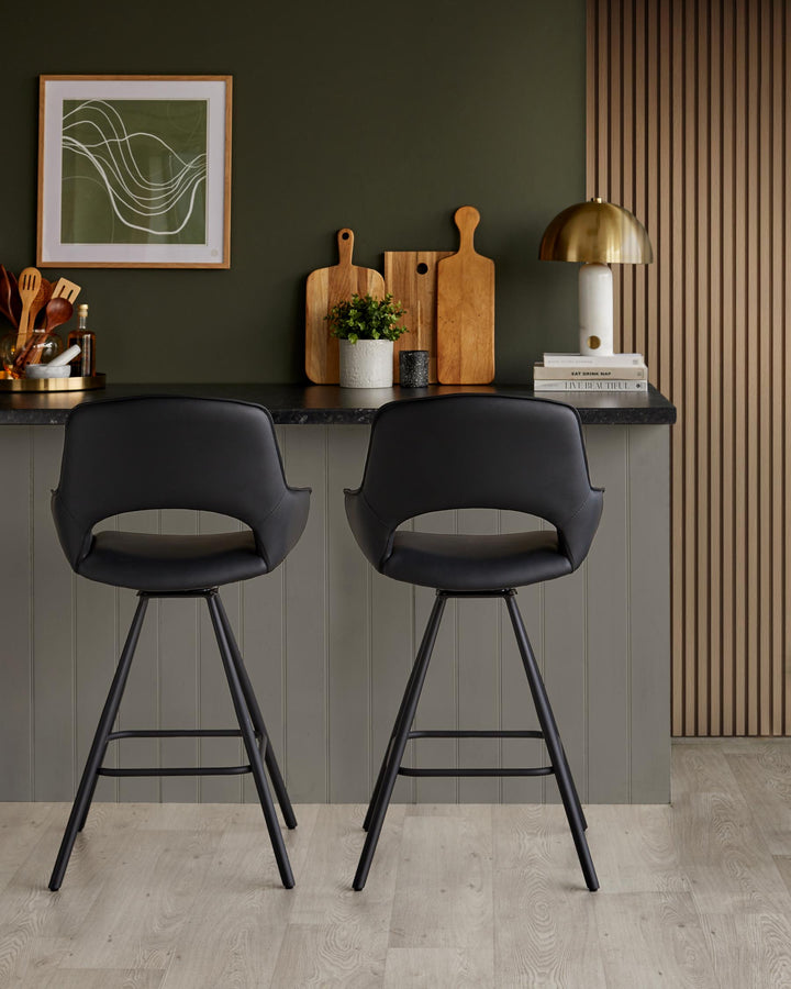 Two black, leather bar stools with black metal legs are positioned at a kitchen island with a dark worktop.