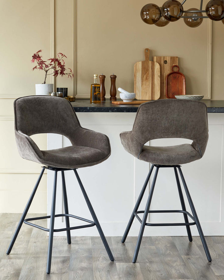 Two swivel bar stools with grey velvet seats and black metal frames stand in front of a kitchen island.