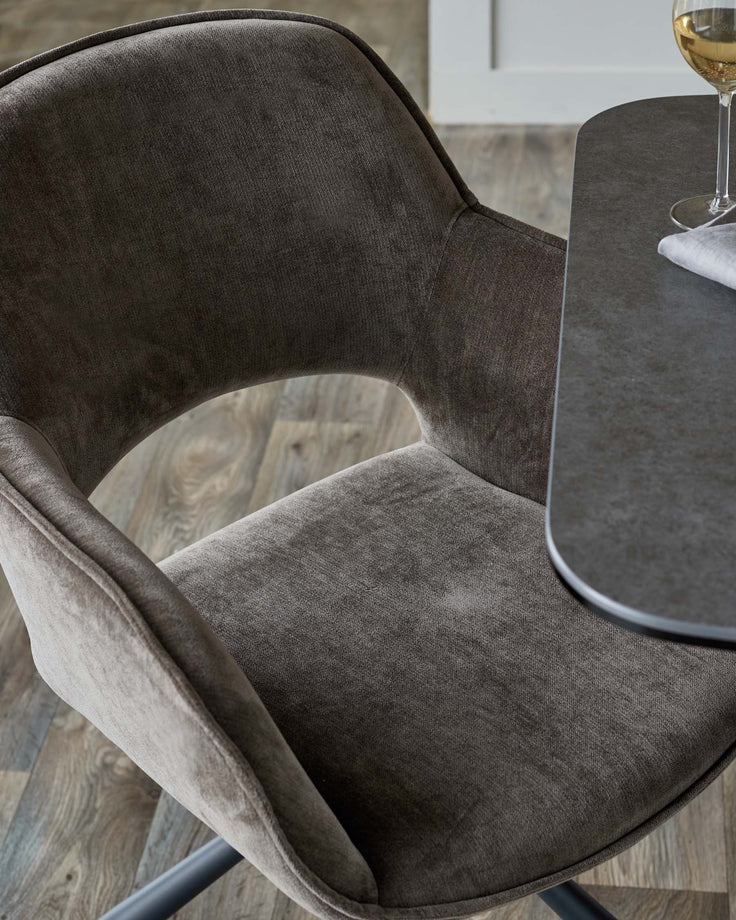 A close-up of a stylish brown fabric chair with a curved back and armrests, paired with a brown table.