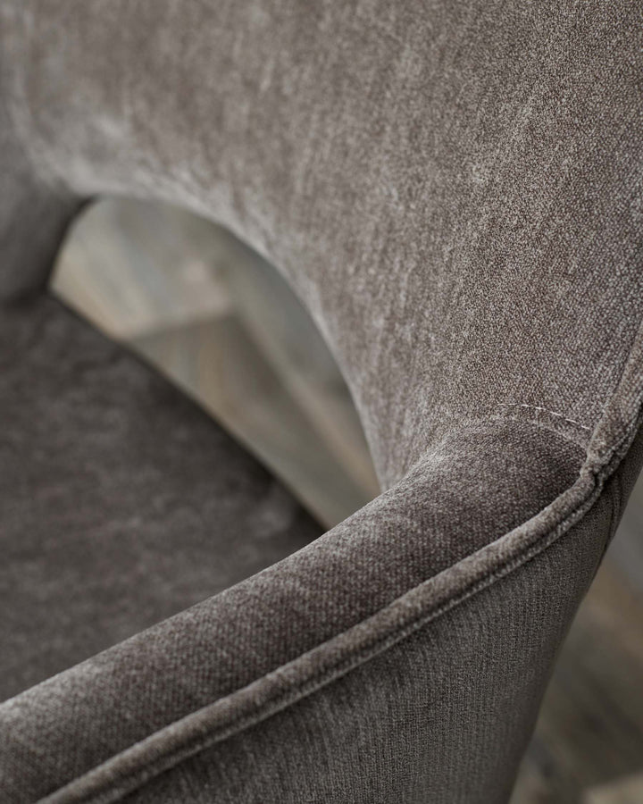 A close-up of a brown upholstered chair, showing the fabric's texture and the chair's curved armrest and back.