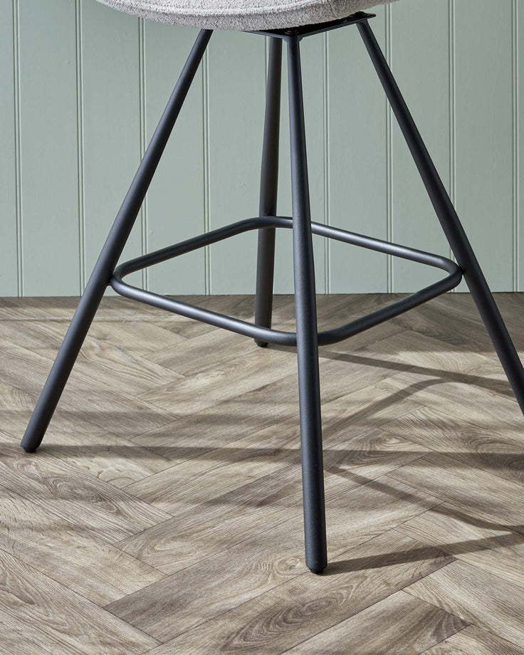 Modern stool with textured light grey upholstered seat and black metal legs on a herringbone pattern wooden floor.