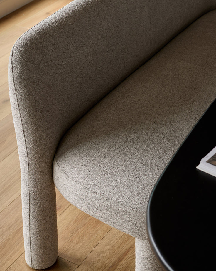 Mason 3-seater dining bench in light grey boucle, curved backrest and cylindrical legs, angled side view.