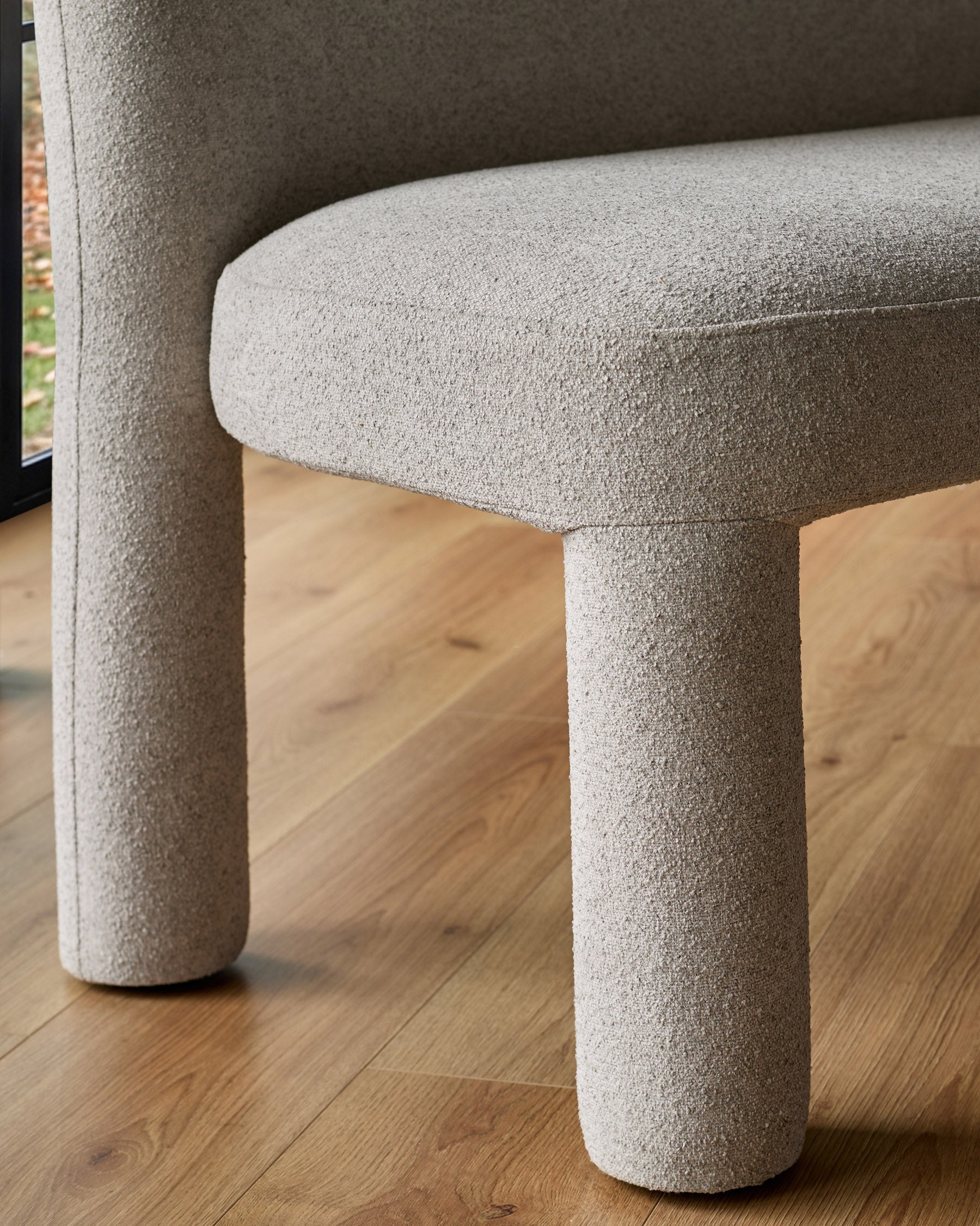Mason 3-seater dining bench in light grey boucle, showing curved cylindrical legs and rounded armrest detail.