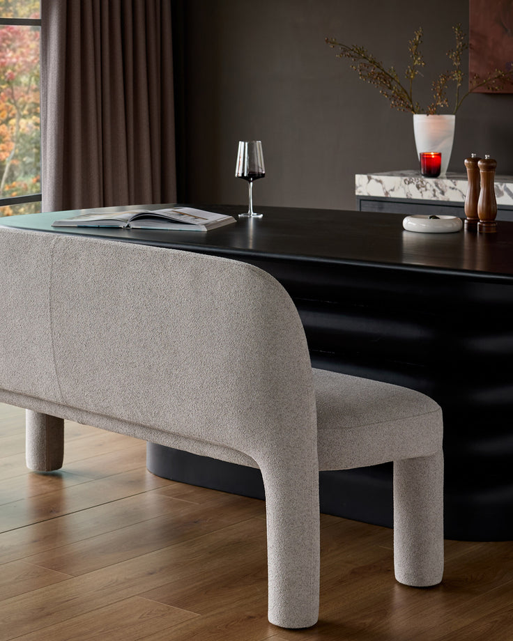 Mason 3-seater dining bench in light grey boucle, featuring curved cylindrical legs and a rounded backrest, positioned at a black table.
