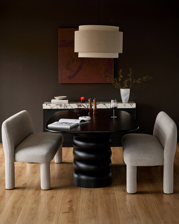 Black round pedestal dining table with cream boucle chairs in modern dining room setting.