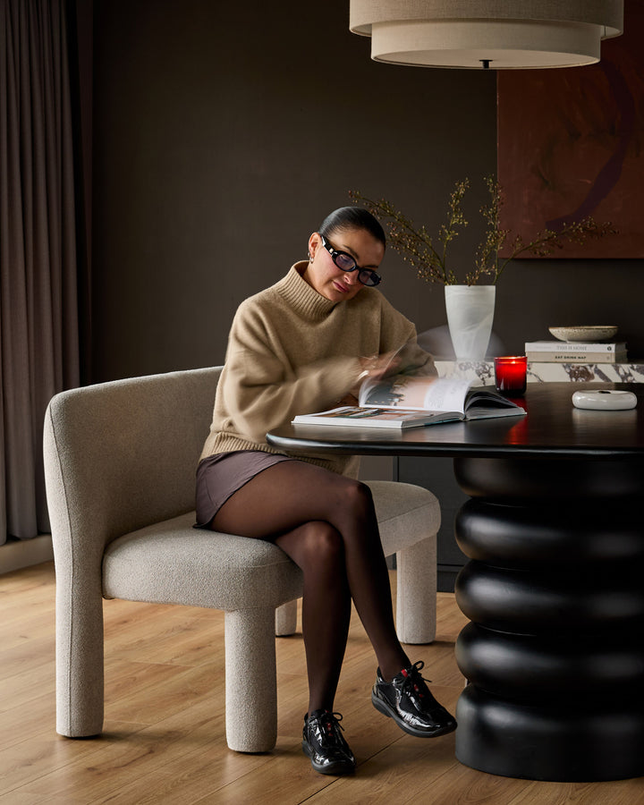 Light grey boucle dining chair with curved, rounded legs, shown in a styled interior setting at a black table.