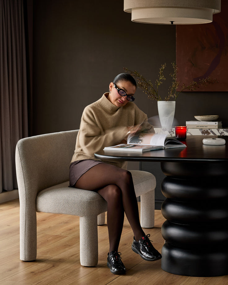 Light grey boucle dining chair with curved, rounded legs, shown in a styled interior setting at a black table.