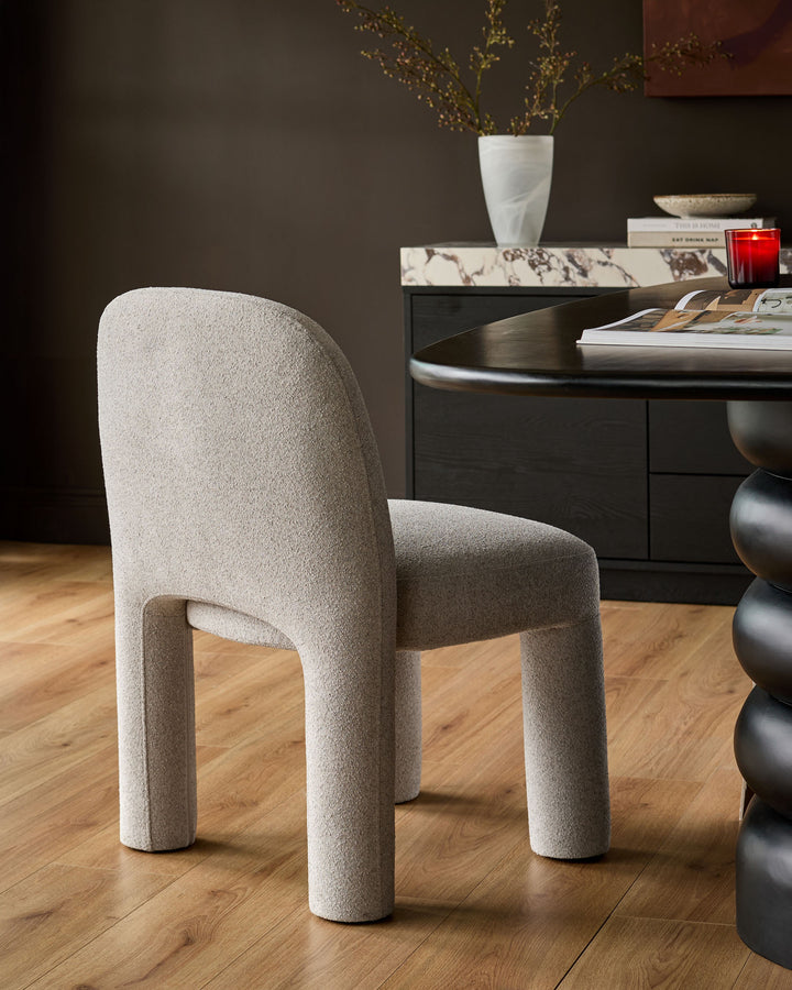 Mason dining chair in light grey boucle, featuring curved cylindrical legs and rounded backrest, shown in a styled room setting.