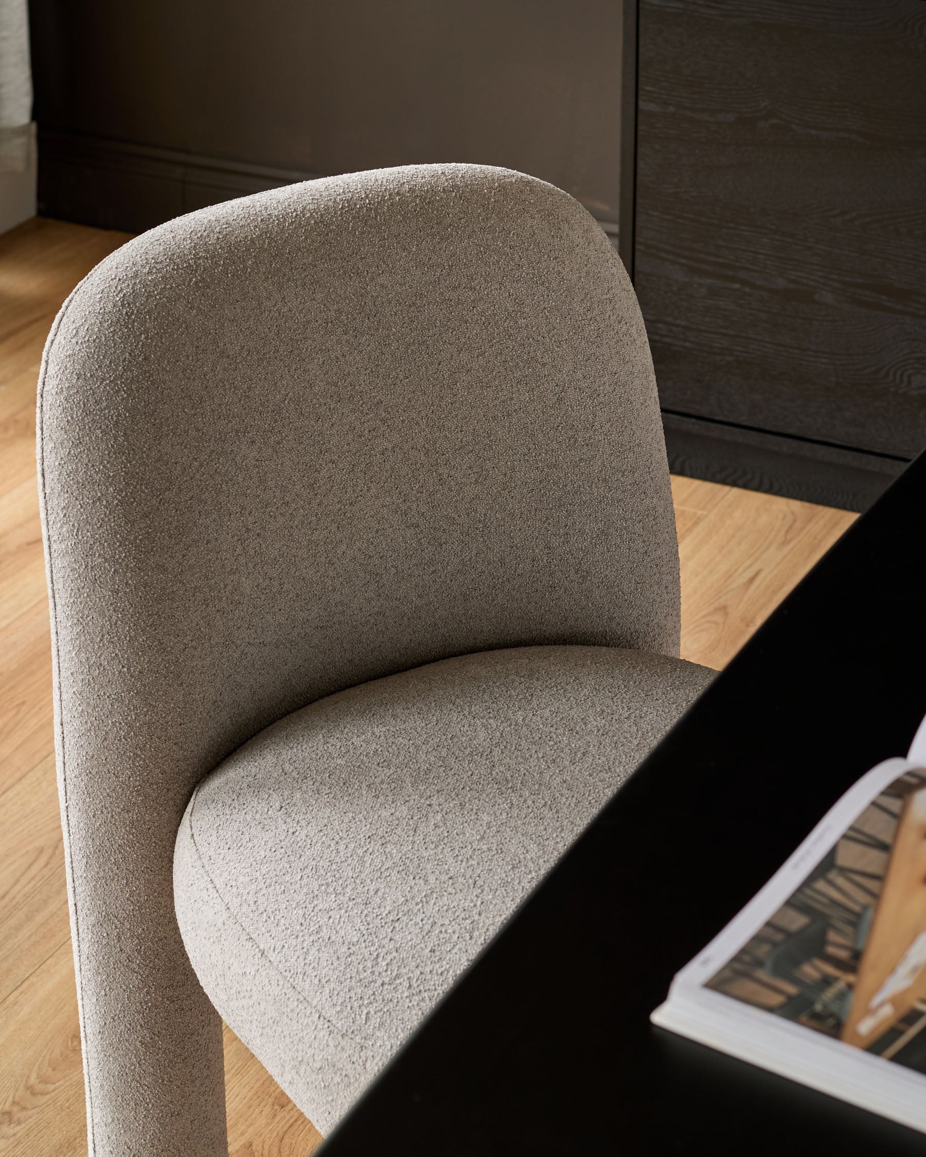 Mason dining chair in light grey boucle, shown at an angle highlighting the curved backrest and seat cushion on wooden flooring.