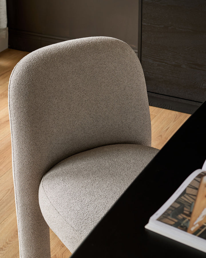 Mason dining chair in light grey boucle, shown at an angle highlighting the curved backrest and seat cushion on wooden flooring.