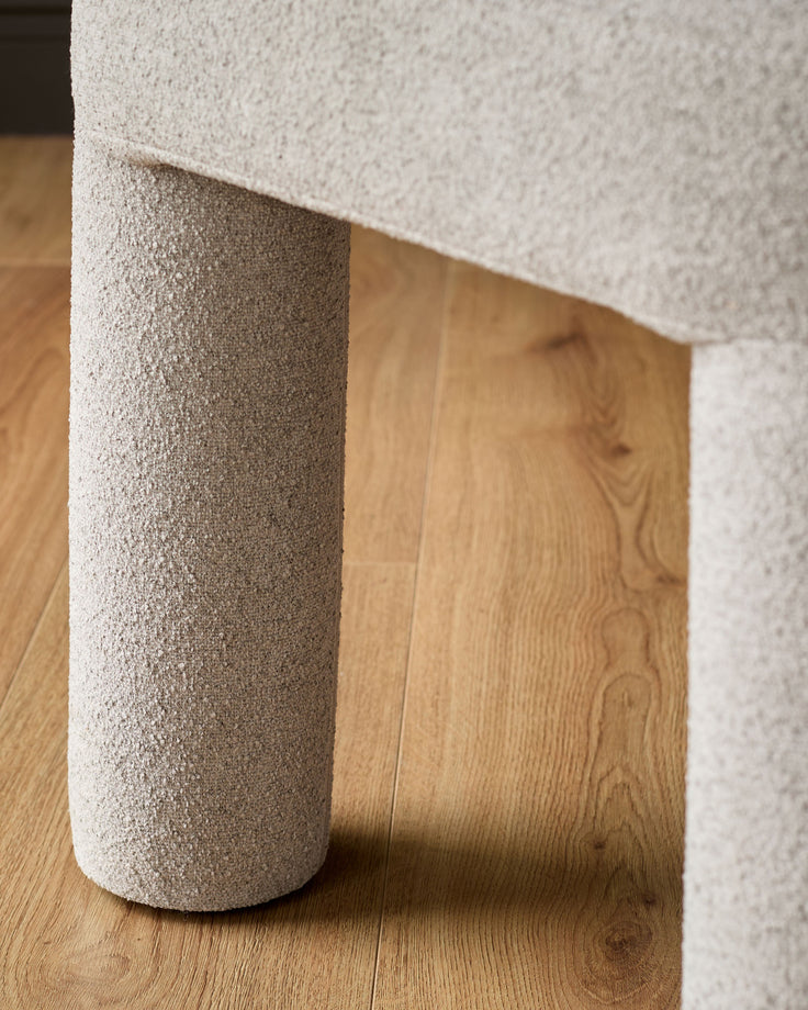 Mason dining chair in light grey boucle, showing cylindrical leg detail on wooden floor.