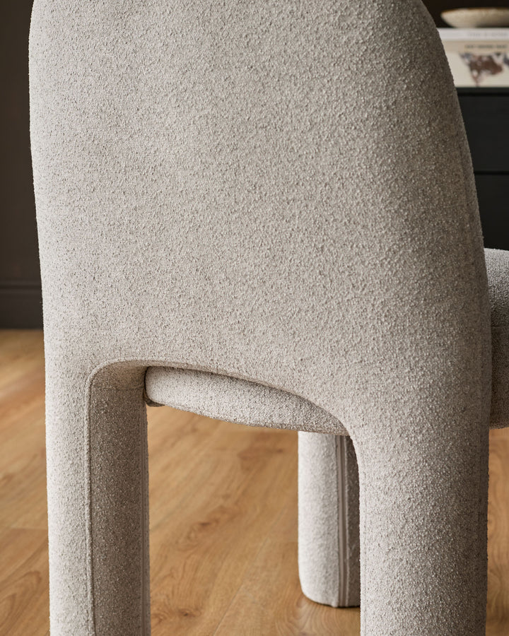 Mason dining chair in light grey boucle, showing curved leg detail and textured fabric finish from side angle.