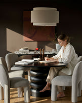 Mason dining chair in light grey boucle, shown at round table with woman writing.