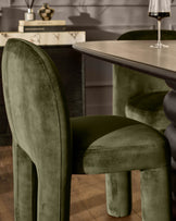 Mason dining chair in olive green velvet, shown from a side angle at a table setting with wine glass.
