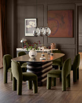 Mason dining chair in olive green velvet, shown in dining room setting around sculptural black table.