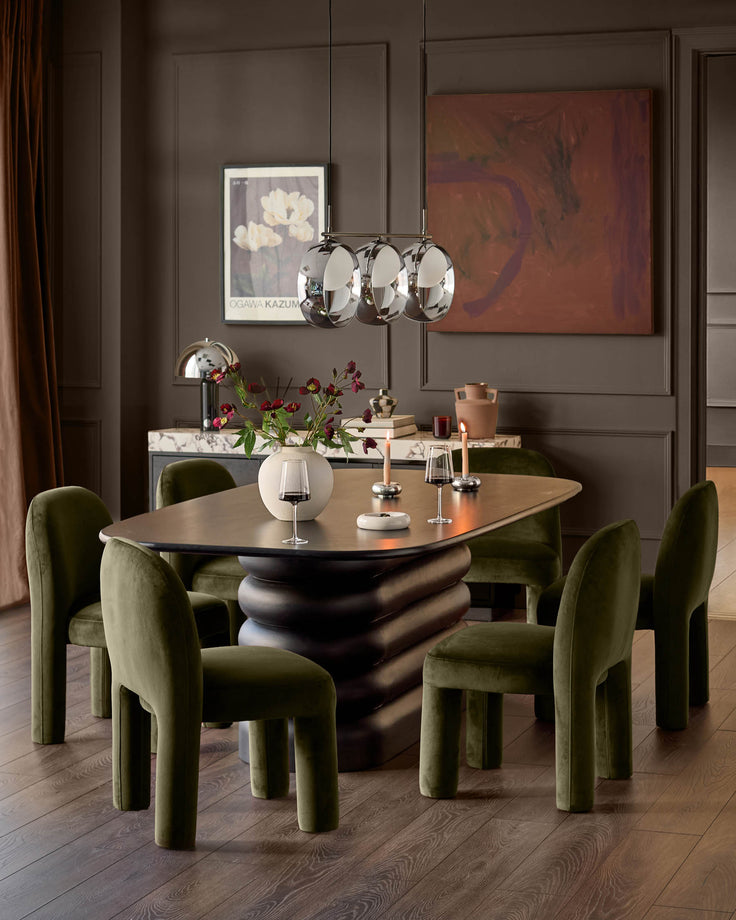 Mason dining chair in olive green velvet, shown in dining room setting around sculptural black table.